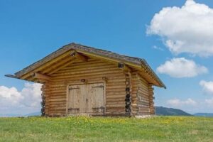 Casetta di legno con tetto spiovente in un prato fiorito sotto il cielo azzurro
