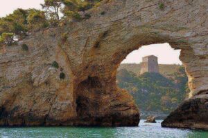 Arco naturale di roccia sul mare con una torre di avvistamento sullo sfondo