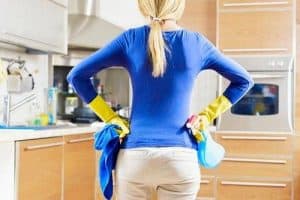 Donna di spalle con guanti da lavoro gialli e panni in mano in una cucina