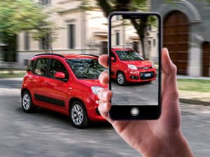 Mano che fotografa con lo smartphone una utilitaria rossa parcheggiata sulla strada